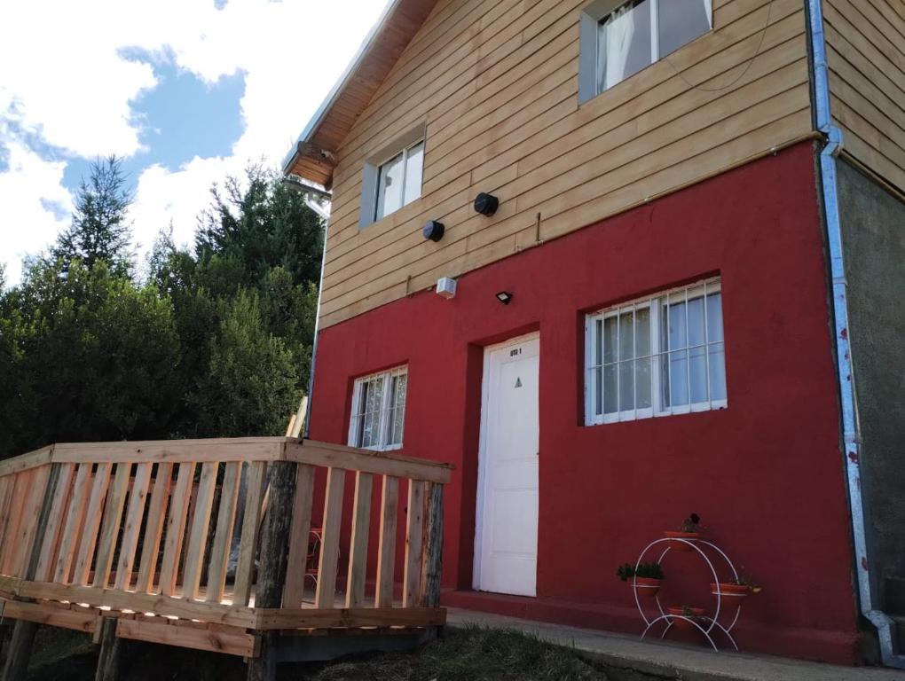een rood huis met een witte deur en een houten veranda bij Unkai Bariloche in Bariloche