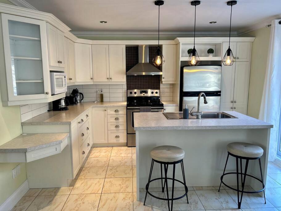 a kitchen with white cabinets and a sink and two bar stools at 3BR House 6 Guests Near Water in Laval