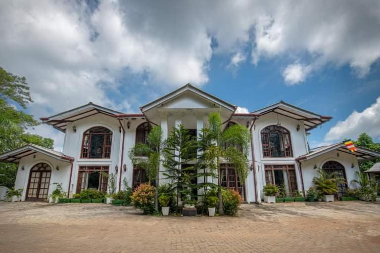 un grand bâtiment blanc avec des plantes devant lui dans l'établissement The Richmond House Kandy, à Kandy