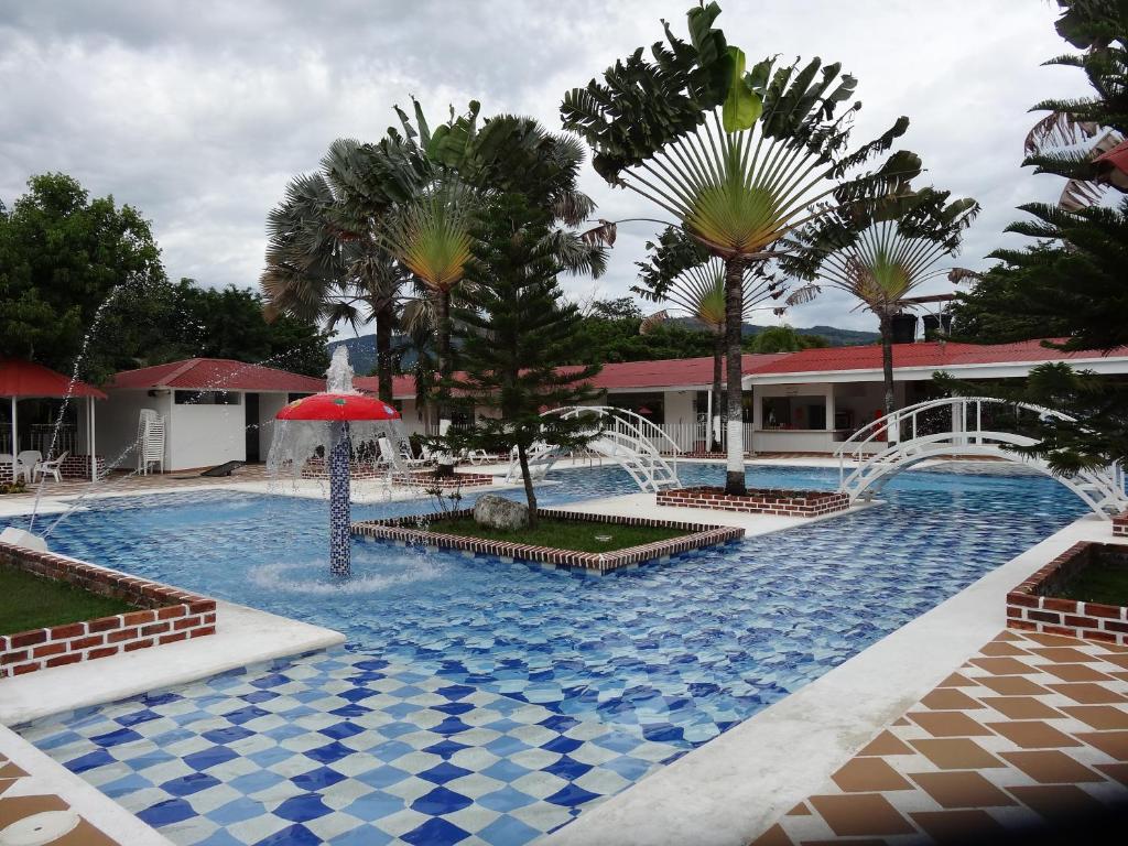 a swimming pool with a red umbrella and palm trees at CENTRO VACACIONAL & HOTEL CAMPESTRE LAGO CENTER in Aguazul