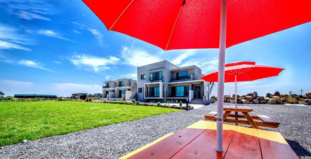 a red umbrella and a bench in front of a house at Boreum Pension in Seogwipo