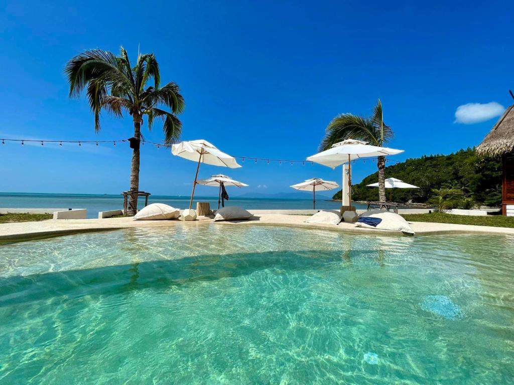 a large swimming pool with umbrellas and the ocean at Le Shelby Samui Beach Resort Cottage in Koh Samui