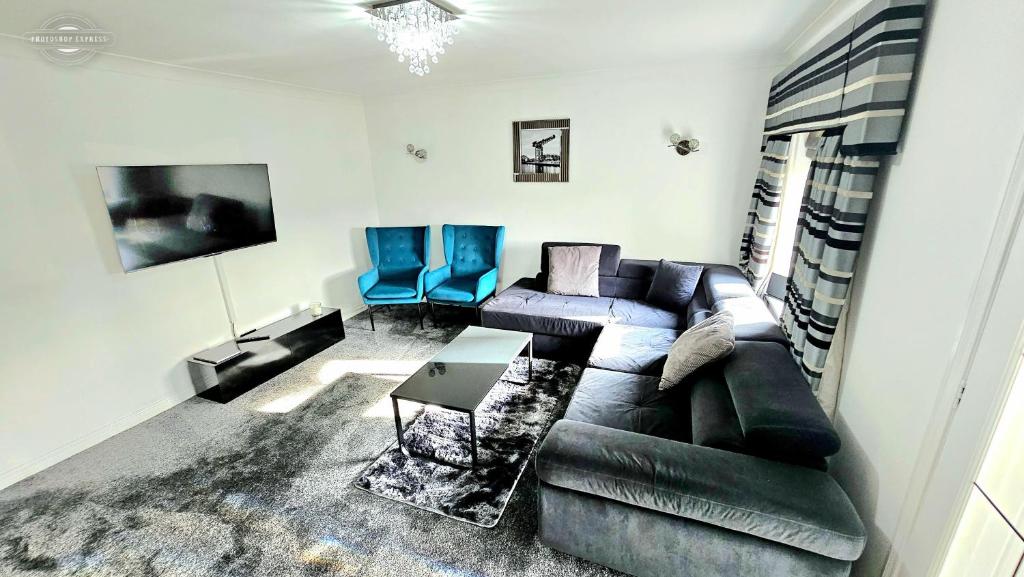 sala de estar con sofá negro y sillas azules en Lovely 3 Bed Home In Glasgow with FREE Parking, en Glasgow