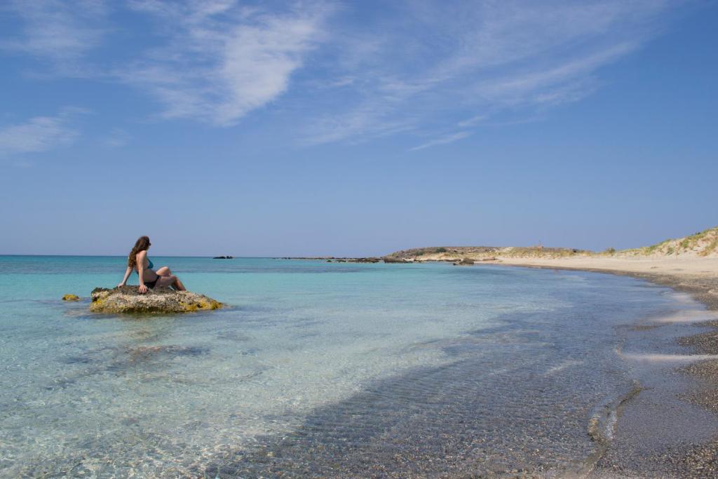 a woman sitting on a rock in the water on a beach at Elafonisi Paradise with Parking, WiFi, - Walking Distance to the Beach in Elafonisi