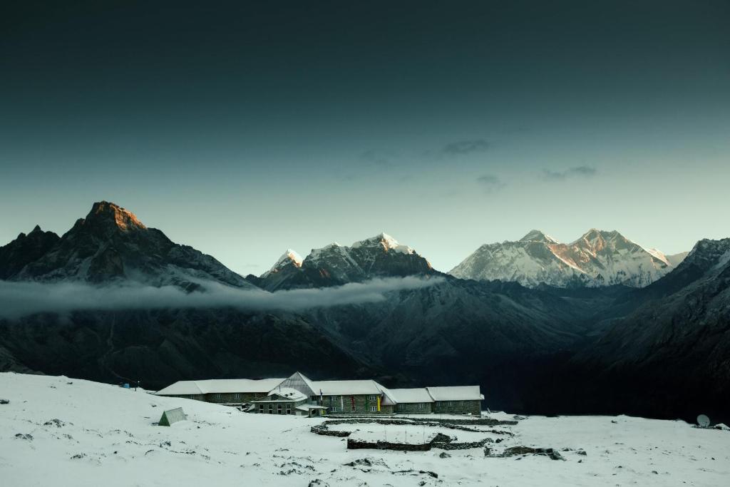 una casa en una montaña nevada con montañas en el fondo en Mountain Lodges of Nepal - Kongde, en Kongde