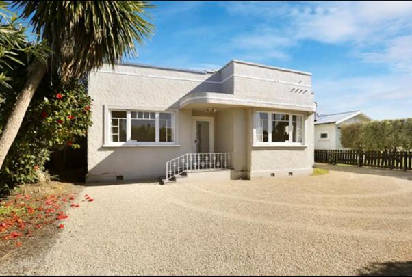a white house with a palm tree and a driveway at Central and Affordable - Cute Art Deco in Gisborne