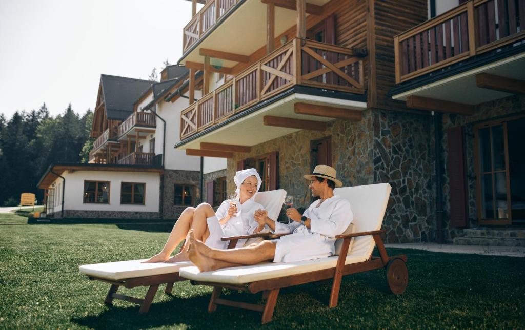 Un uomo e una donna seduti su una sedia a sdraio di Pohorje Village Wellbeing Resort - Family Apartments Bolfenk a Hočko Pohorje