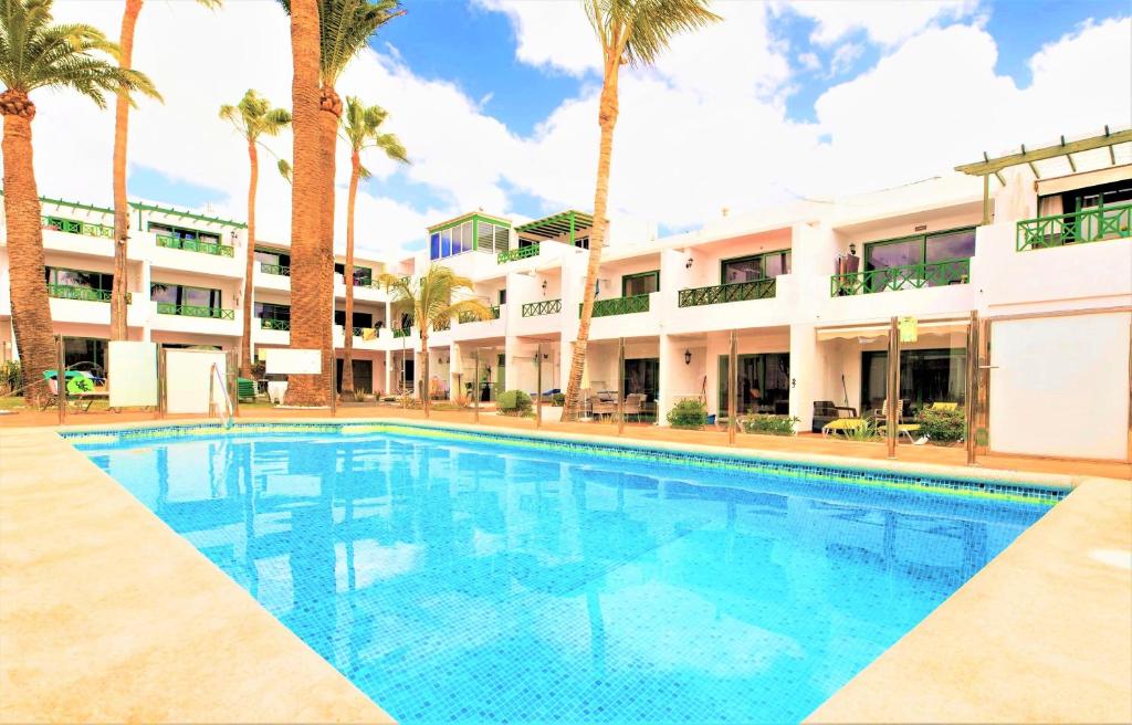 a swimming pool in front of a building with palm trees at Beautiful One Bedroom Ground Floor Apartment - VeraLuna in Tías