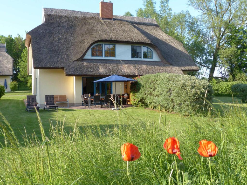 a thatched cottage with red flowers in the yard at Behagliches Reetdachhaus Eibe 1 in Puddemin