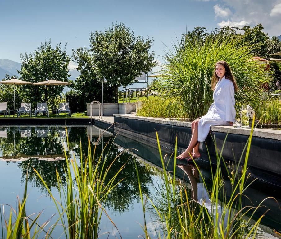 a woman sitting on a ledge next to a pond at Gardenhotel Crystal - 4 Sterne Superior in Fügen