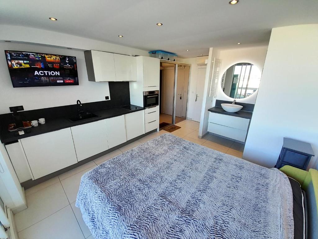 Il comprend une cuisine avec des placards blancs et une télévision murale. dans l'établissement Studio Village Naturiste O Plaisir, au Cap d'Agde