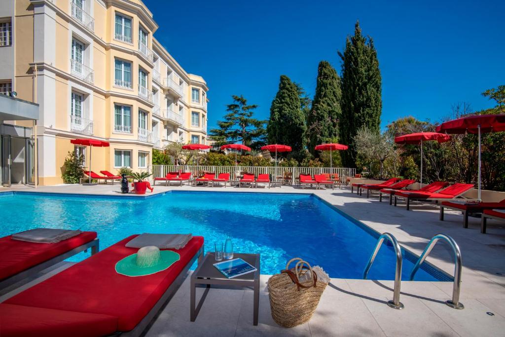 a swimming pool with red chairs and a building at Hotel Carlton in Beaulieu-sur-Mer