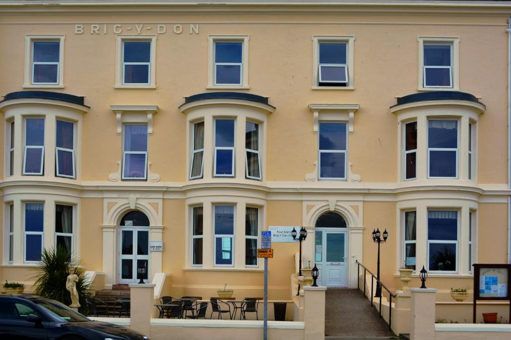 un grand bâtiment jaune avec des tables et des chaises devant lui dans l'établissement Four Saints Brig Y Don Hotel, à Llandudno