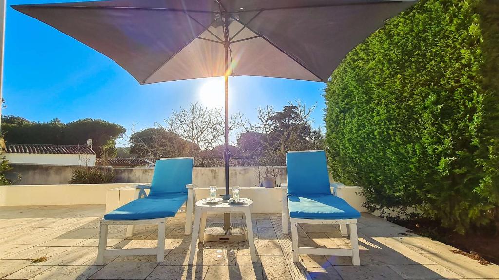 Duas cadeiras e uma mesa com um guarda-sol num pátio em A proximité de la plage et du centre village, villa tout confort em Le Bois-Plage-en-Ré