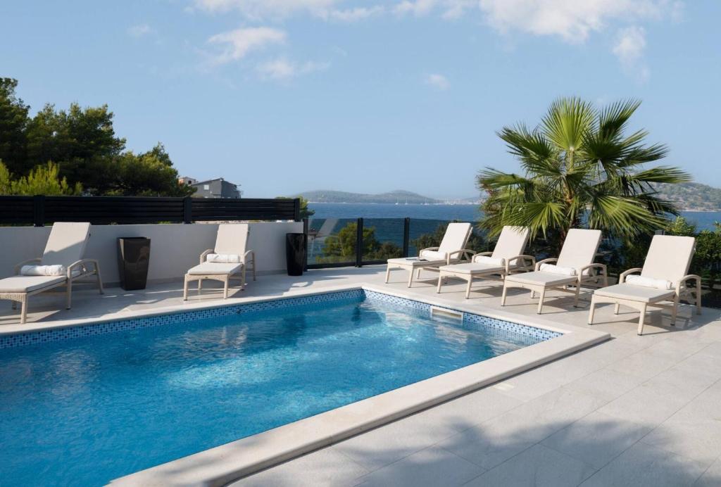 a swimming pool with chairs and the ocean in the background at Villa Palm Bay 1, heated pool - 5 m from the sea in Ražanj
