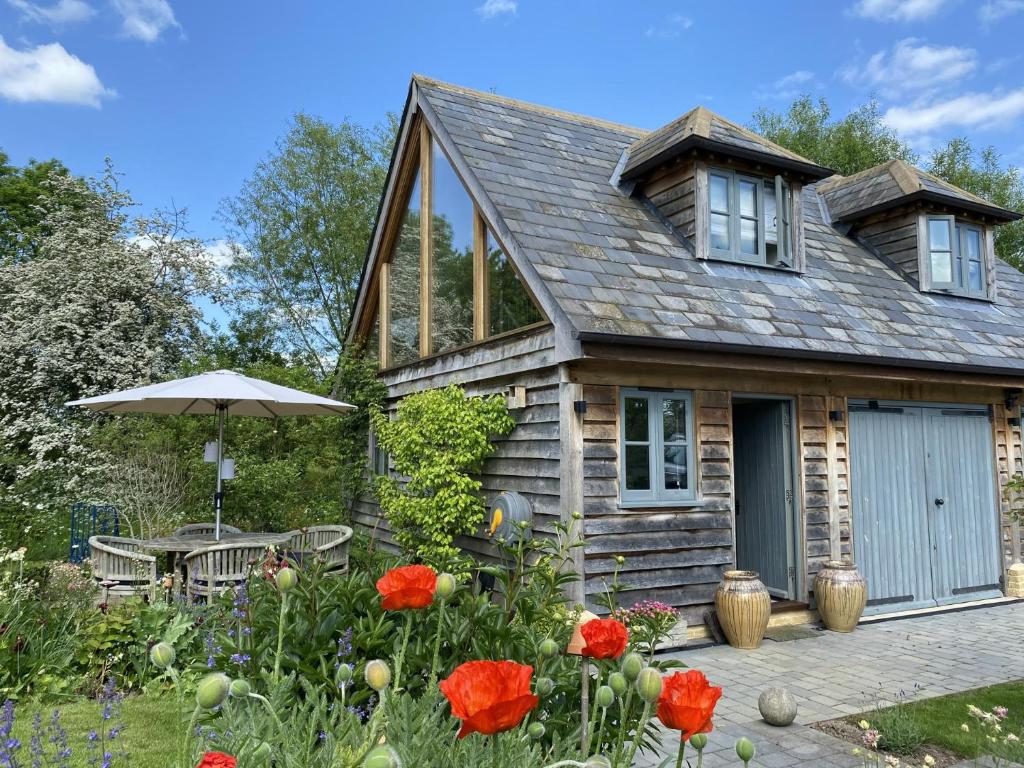 a cottage with a table and an umbrella and flowers at Luxurious Oak Barn in Cotswold Countryside in Shipston-on-Stour