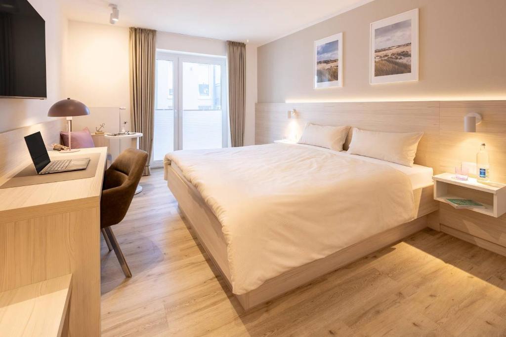 a bedroom with a bed and a desk with a laptop at Hotel Stranddistel in Norderney
