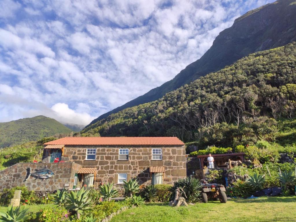 a stone house with mountains in the background at Caldeira Guesthouse in Fajã da Caldeira de Santo Cristo
