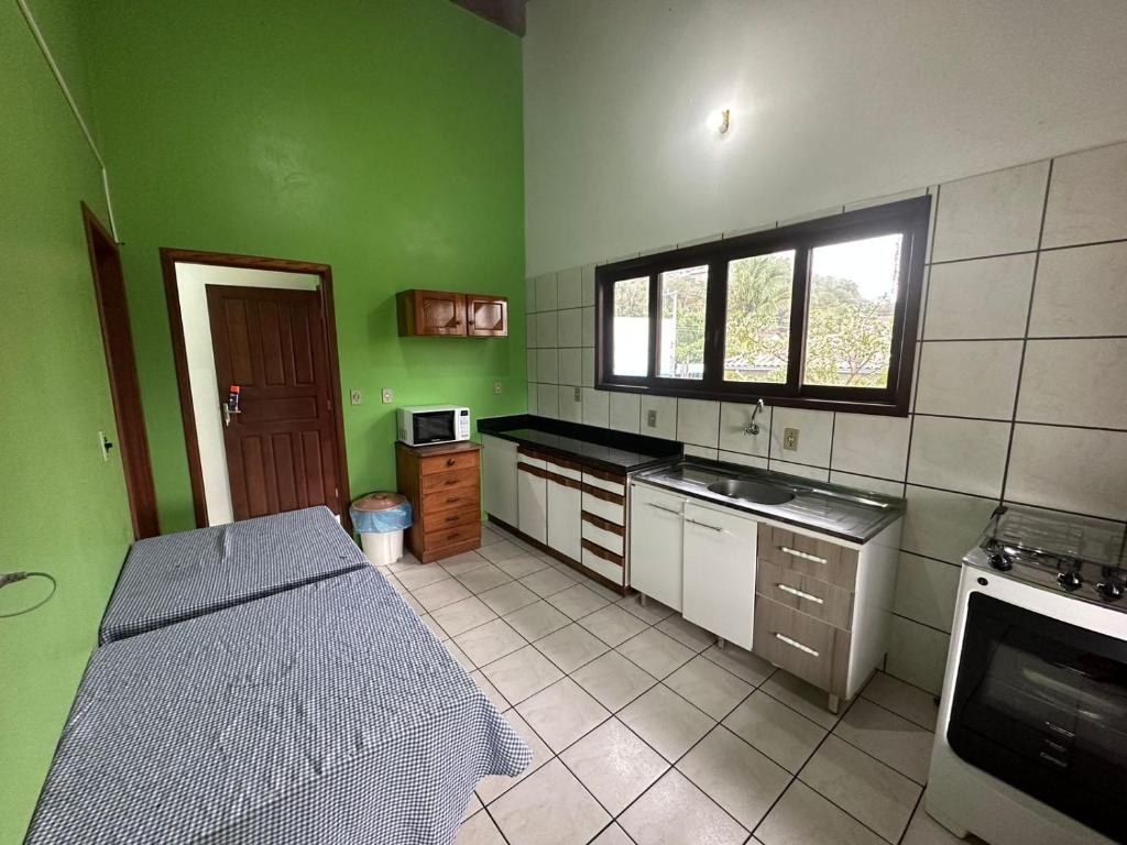 uma cozinha com paredes verdes e uma cama num quarto em Pousada Via Ferrugem em Garopaba