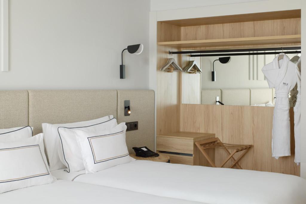 a bedroom with a bed with white pillows and a dress hanging up at Meliá Lloret de Mar in Lloret de Mar