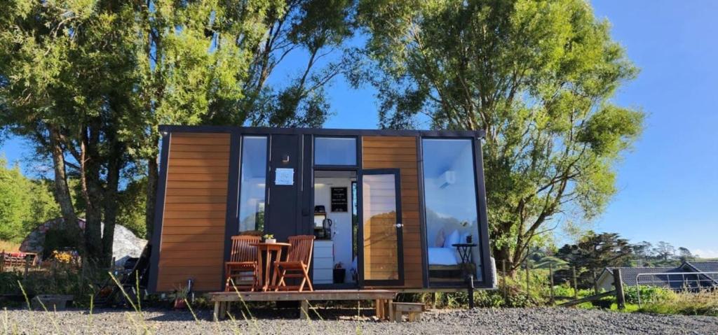 eine kleine Hütte mit einem Tisch und Stühlen vor Bäumen in der Unterkunft Dairy Flat Farm Cabin 1 in Waitoki