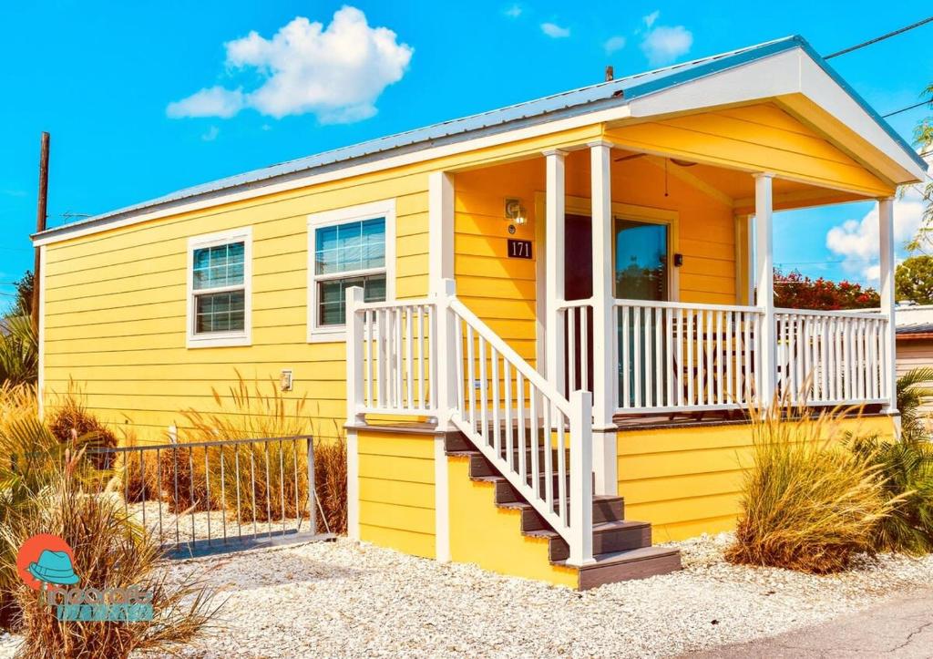 une petite maison jaune avec une véranda blanche dans l'établissement Pinecraft Tiny Home 2, à Sarasota