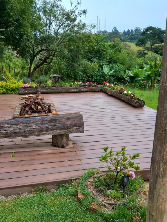 une terrasse en bois avec un foyer extérieur et des fleurs dans l'établissement Rancho dos Pássaros Amarelos, à Campestre