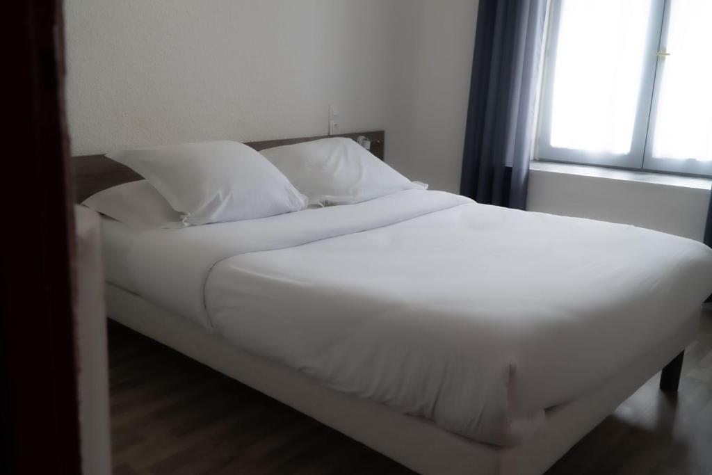 a bed with white sheets and pillows next to a window at Cit'Hotel du Tigre in Verdun-sur-Meuse