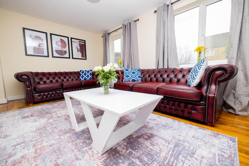 Great Oakley的住宿－Charming 4-bedroom home in Corby，客厅配有红色皮革沙发和白色桌子