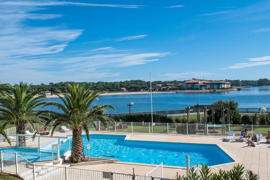 a swimming pool with palm trees and a body of water at Le Boucanier in Vieux-Boucau-les-Bains