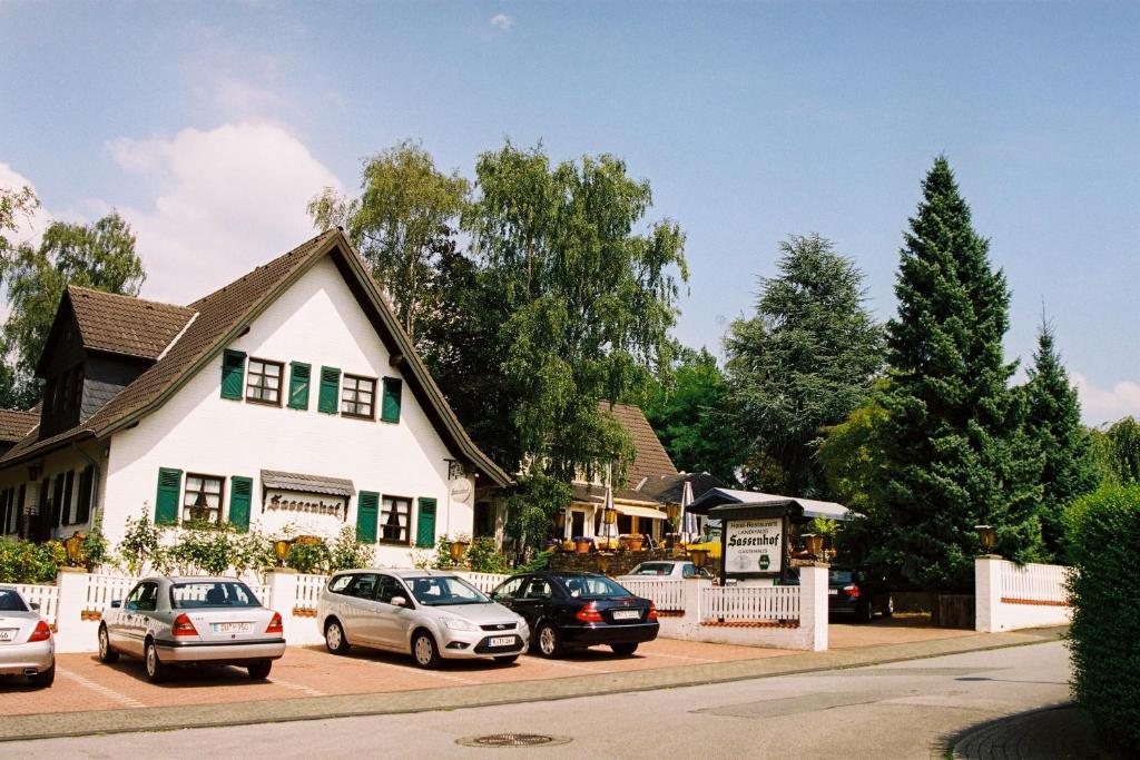 een wit huis met auto's geparkeerd op een parkeerplaats bij Landhaus Sassenhof in Mülheim an der Ruhr