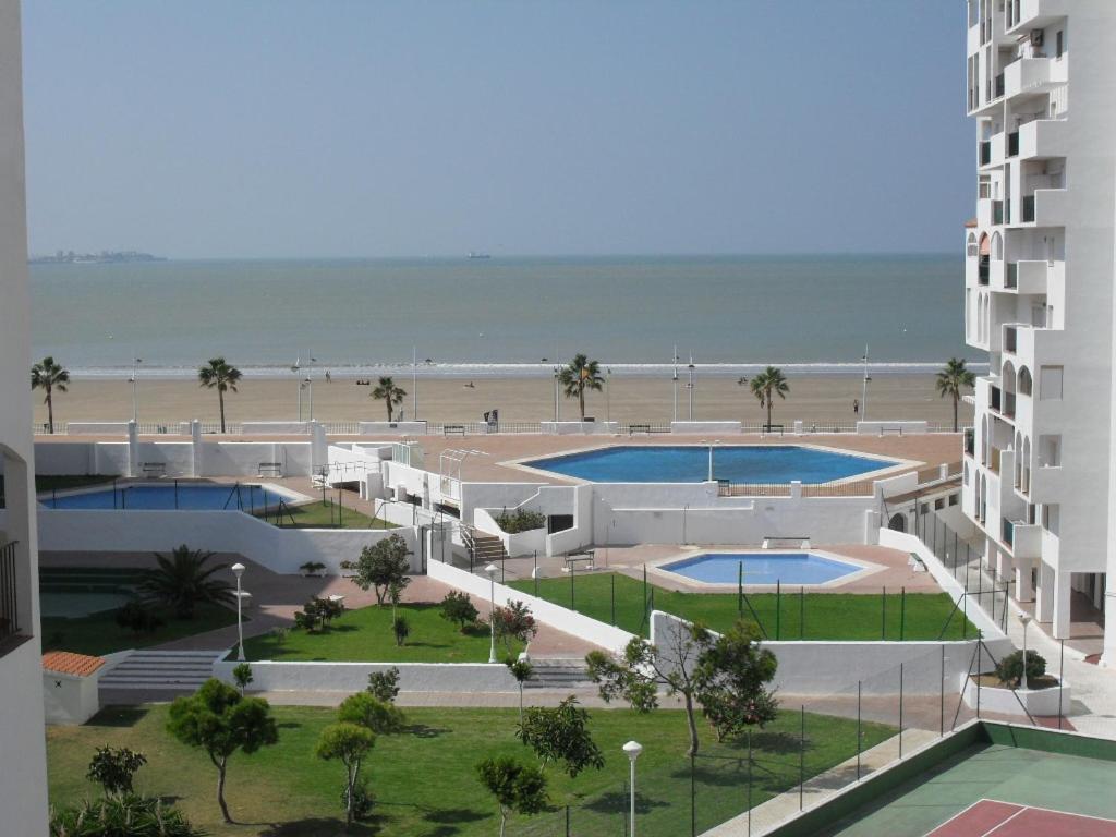 - une vue sur un bâtiment et une plage avec 2 piscines dans l'établissement Navegante, à El Puerto de Santa María