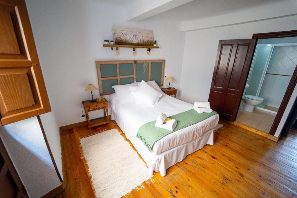 um quarto com uma grande cama branca e pisos em madeira em La bodega D'leti em Jarandilla de la Vera