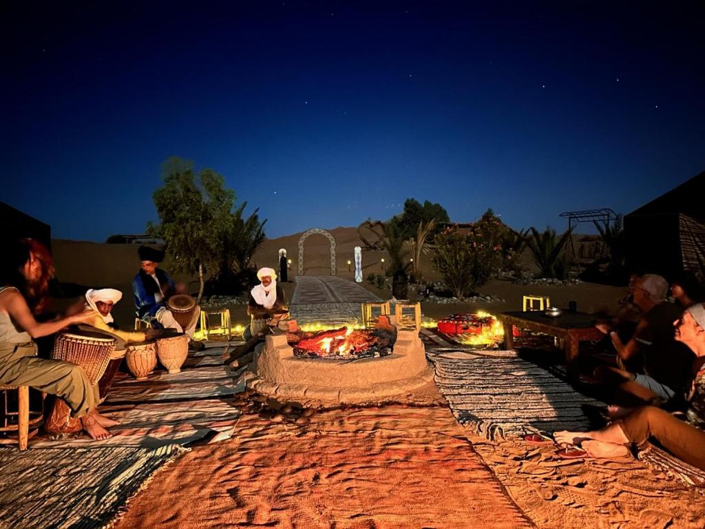 eine Gruppe von Menschen, die um eine Feuerstelle herum sitzen in der Unterkunft Sahara wellness camp in Merzouga