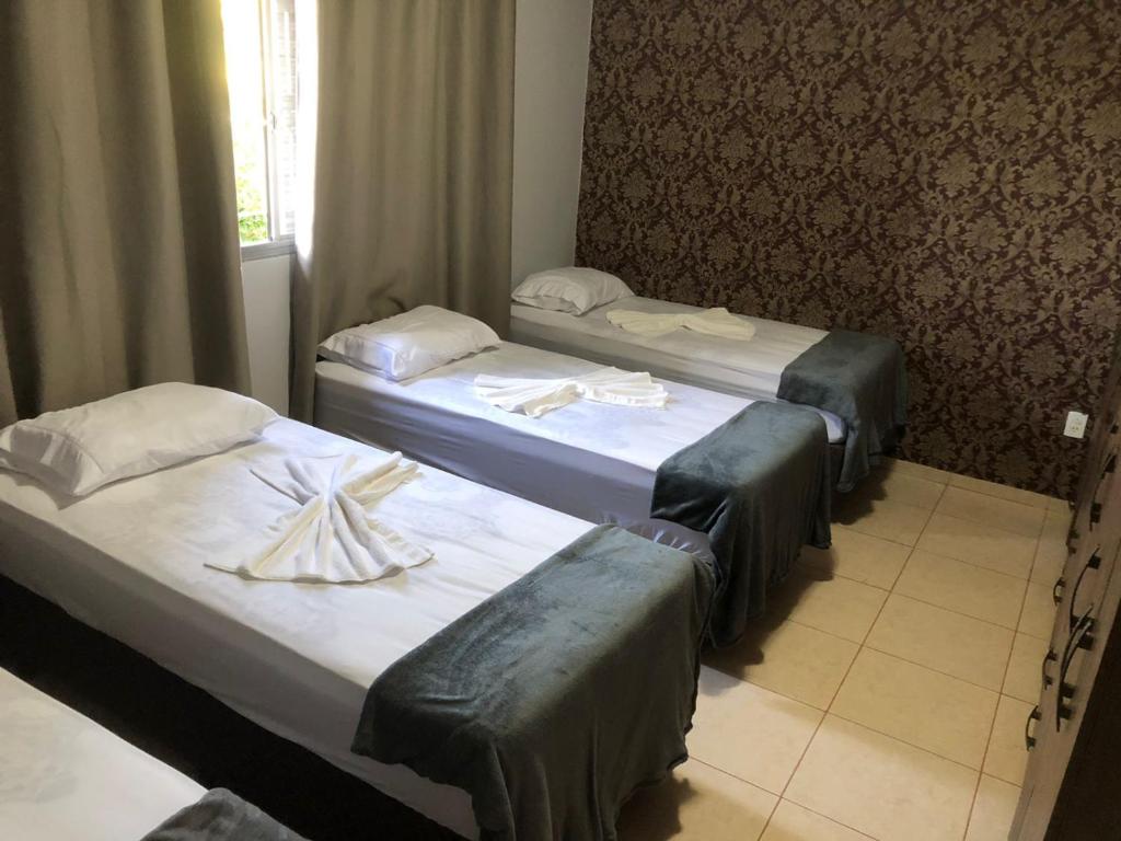 drie bedden in een hotelkamer met handdoeken erop bij Pousada Abba Pai in Maracaju