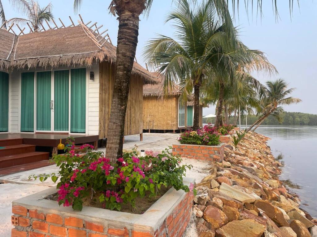 Nov Koh Kong Resort في Phumĭ Srê Thmei: بيت فيه نخله وزهور بجانب الماء