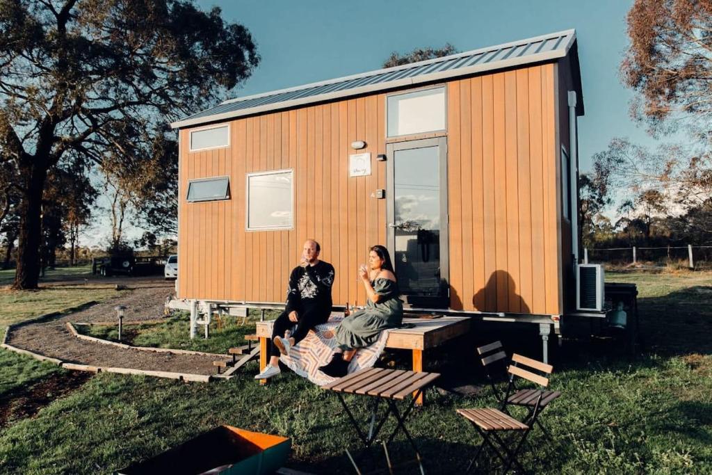 Un uomo e una donna seduti di fronte a una casetta di Odyssean Tiny House a Cessnock