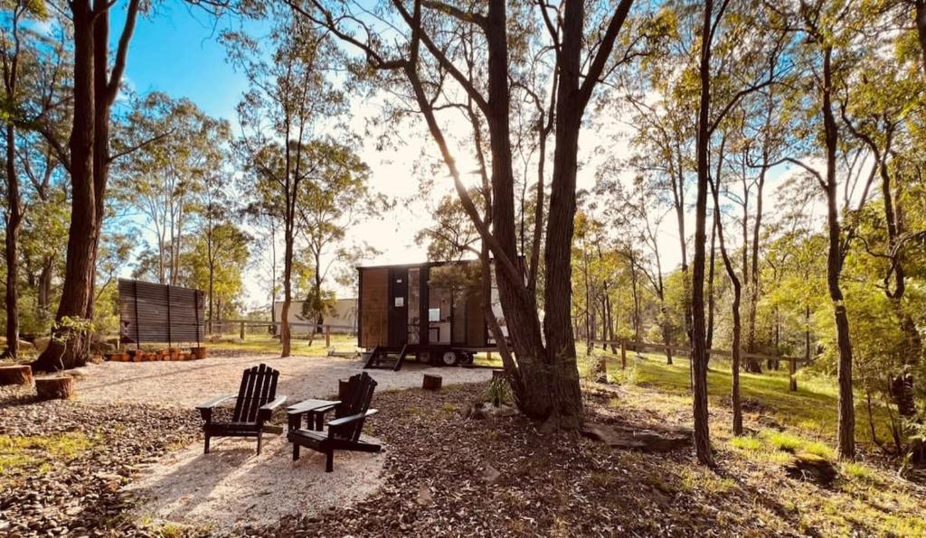 a house sitting in a park with two benches at Kawal Tiny House in Wollombi