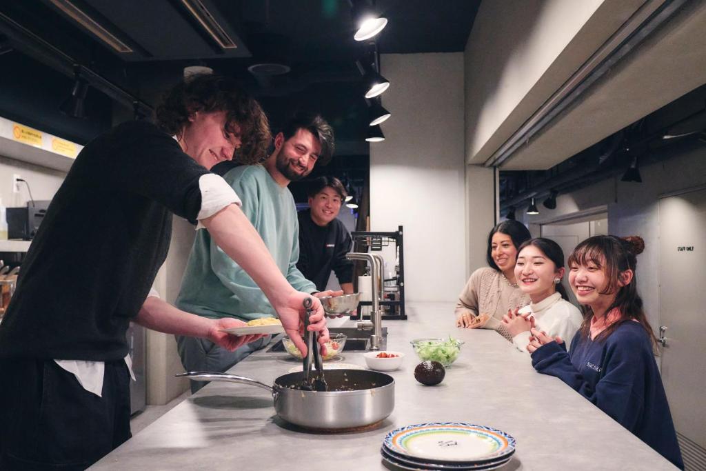 a man preparing food in a kitchen with a group of people at &AND HOSTEL SHINSAIBASHI EAST in Osaka