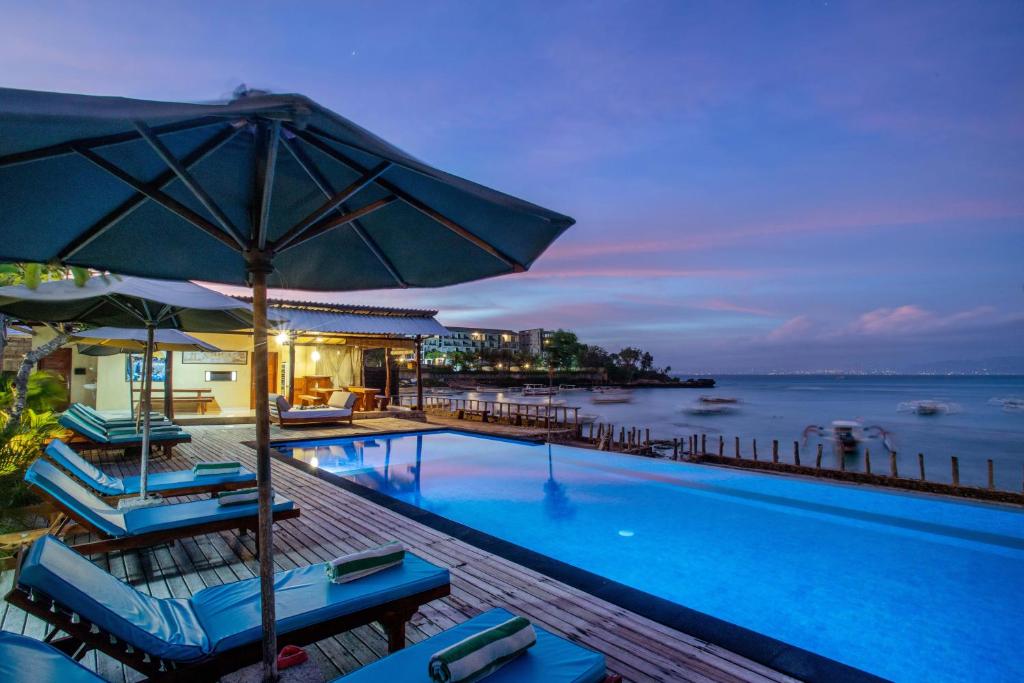 een zwembad met stoelen en een parasol bij D'Muncuk Huts Lembongan in Nusa Lembongan