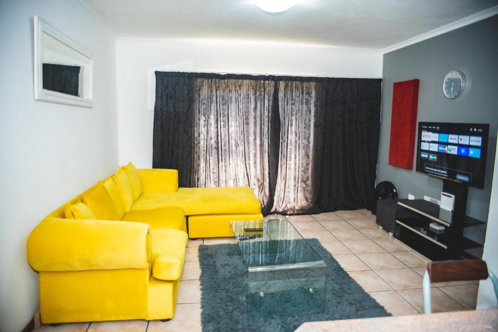a living room with a yellow couch and a television at Ankazimia House at Reeds View in Roodepoort