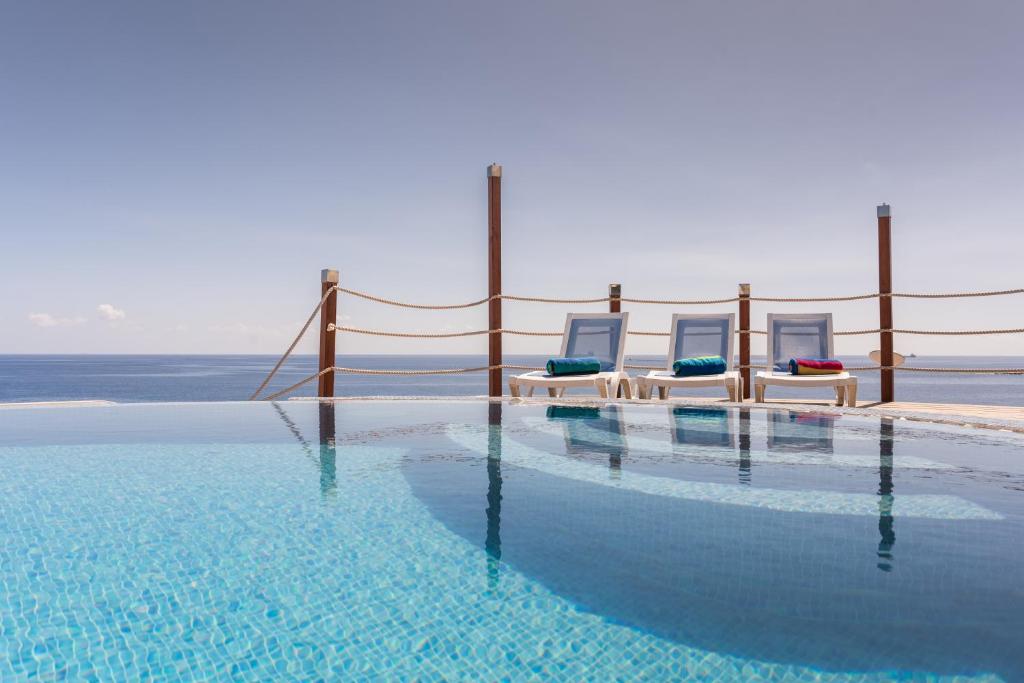 a swimming pool with two chairs and the ocean at Waters-Edge Complex in Marsaskala