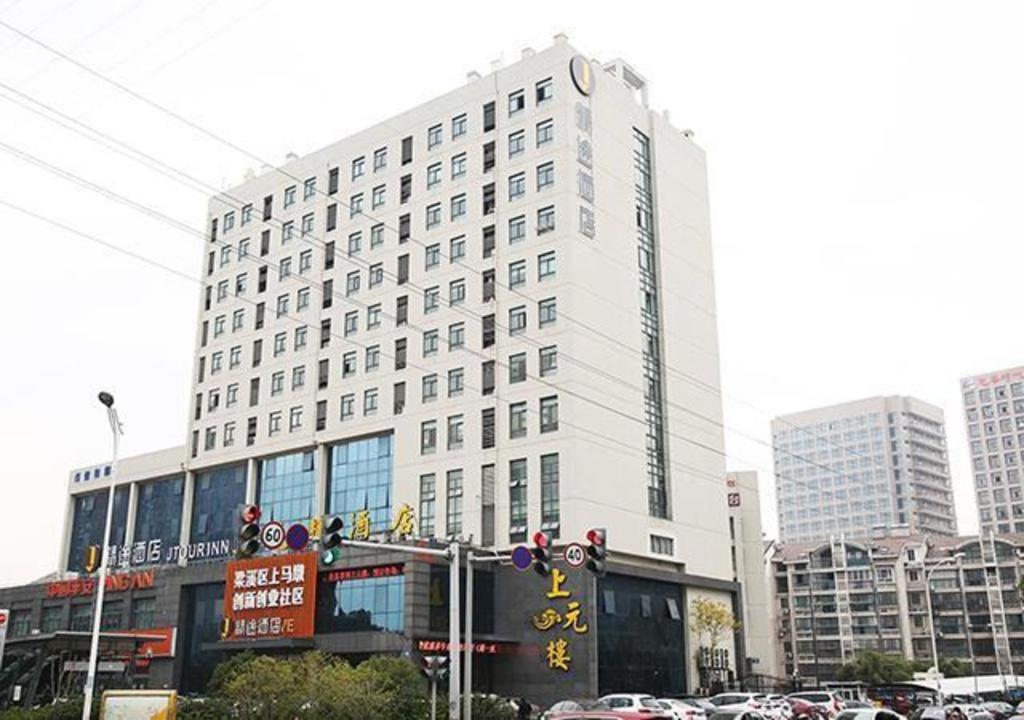 a tall white building with cars parked in front of it at JTOUR Inn Wuxi Railway Station Shangmadun Metro Station in Wuxi