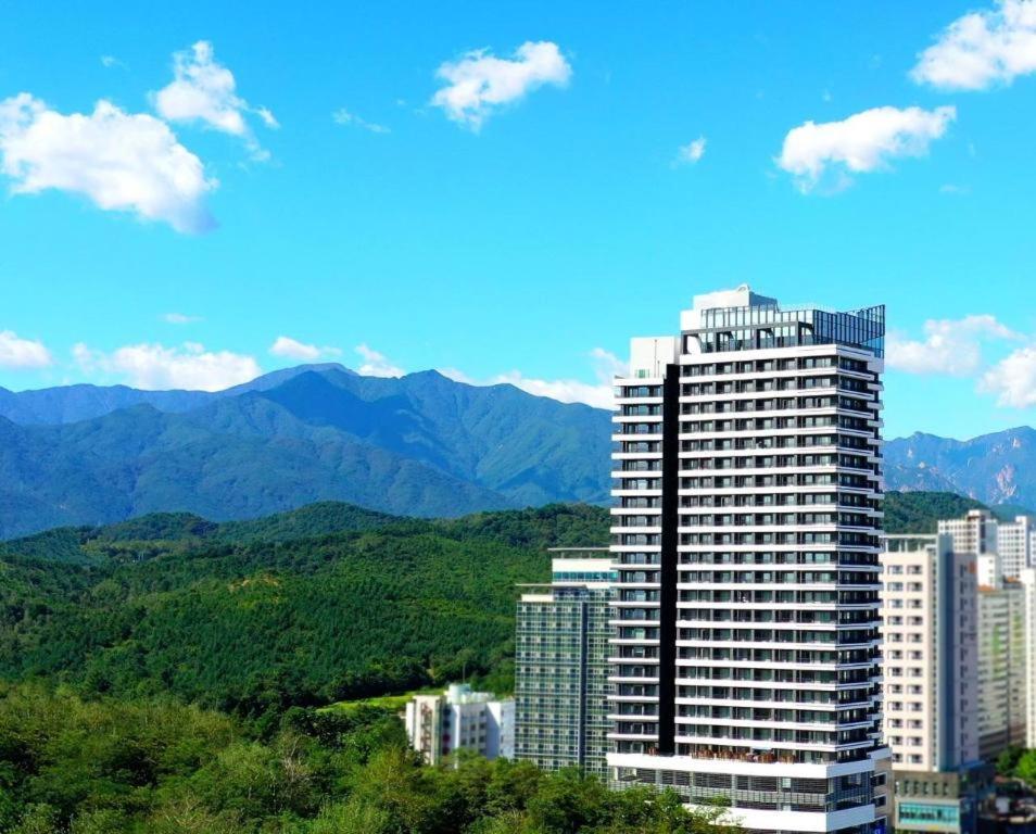 un edificio alto con montañas en el fondo en The BlueMark Hotel Sokcho en Sokcho