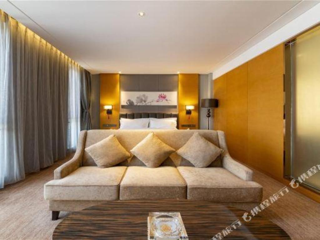 a living room with a couch in front of a bed at Borrman Hotel Jinan Yijia Exhibition Center Laotun Metro Station in Jinan