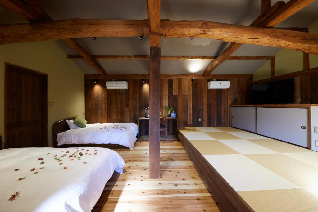 two beds in a room with wooden floors and wooden beams at ゲストハウス長閑 in Toyooka
