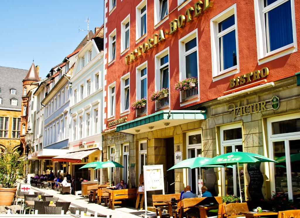 eine Straße mit Tischen und Sonnenschirmen vor einem Gebäude in der Unterkunft Victoria Hotel in Minden