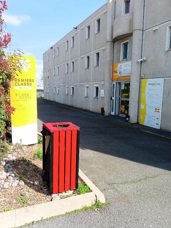 a red trash can sitting on the side of a street at Premiere Classe Saint Brice Sous Foret in Saint-Brice-sous-Forêt