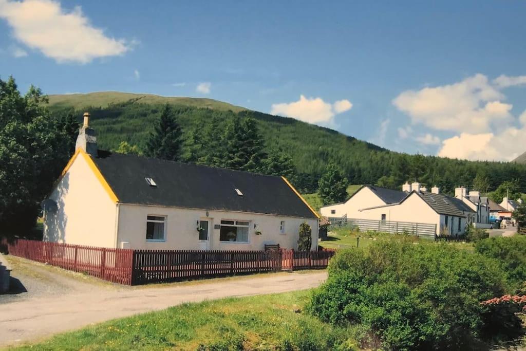 a white house with a black roof and a fence at Cosy Highland Cottage Tyndrum centrally located in Tyndrum