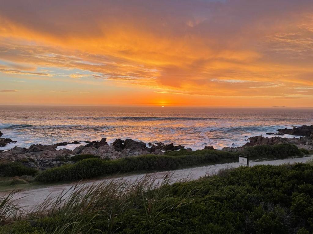 una puesta de sol sobre una playa con el océano en Pondjiebotter, en Pringle Bay